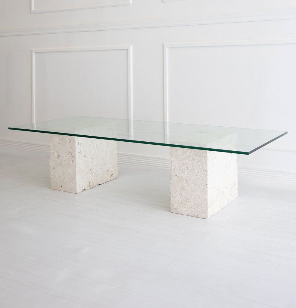 Glass coffee table with two natural stone legs against a white wall background